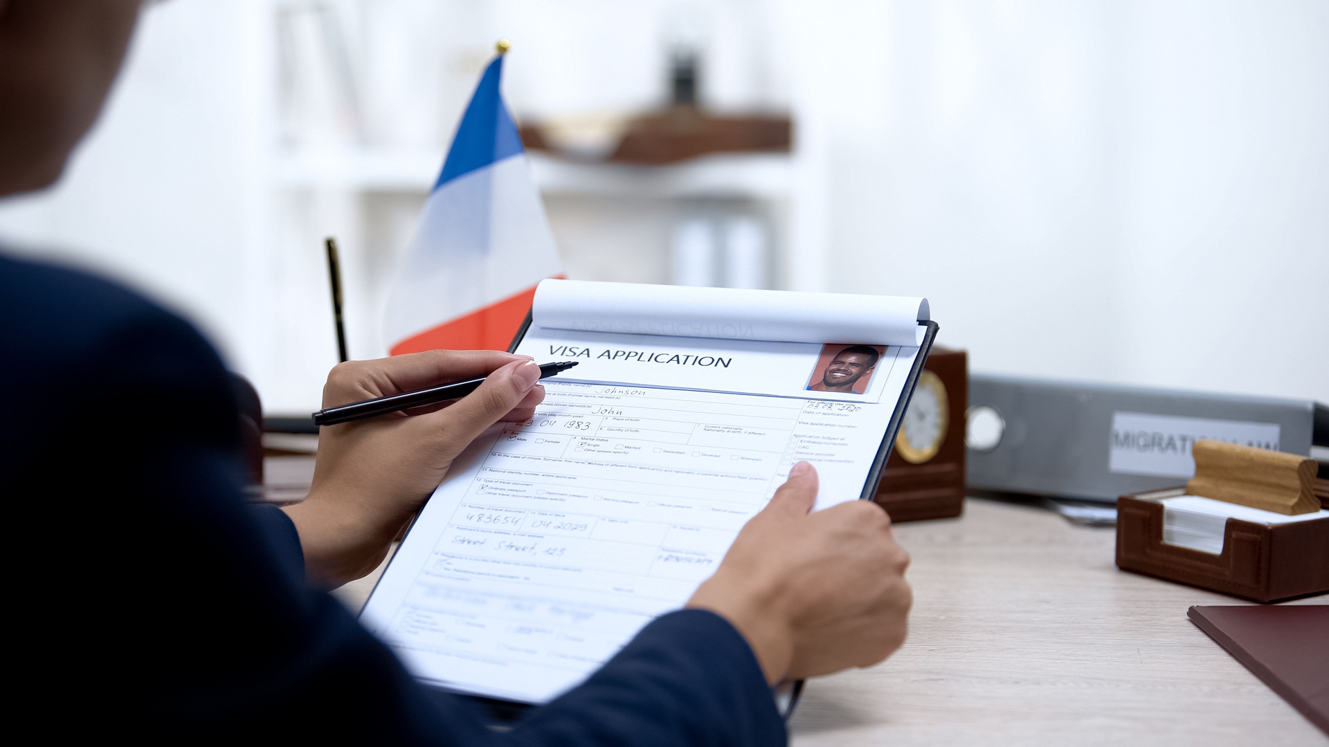 A person reviewing a visa application form at a desk next to a small French flag.