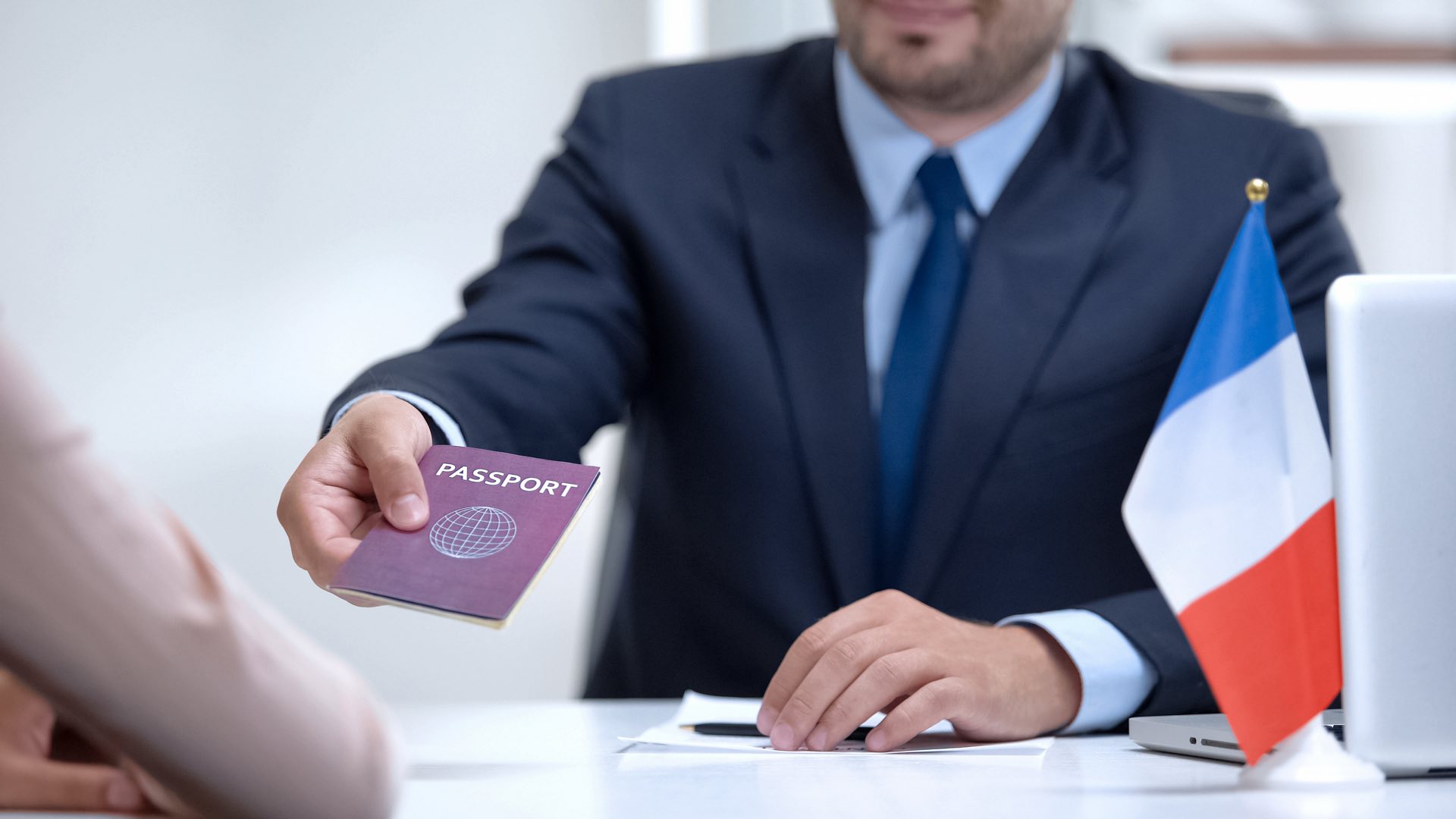 Business man in blue suit at a desk handing a passport across the table to another person