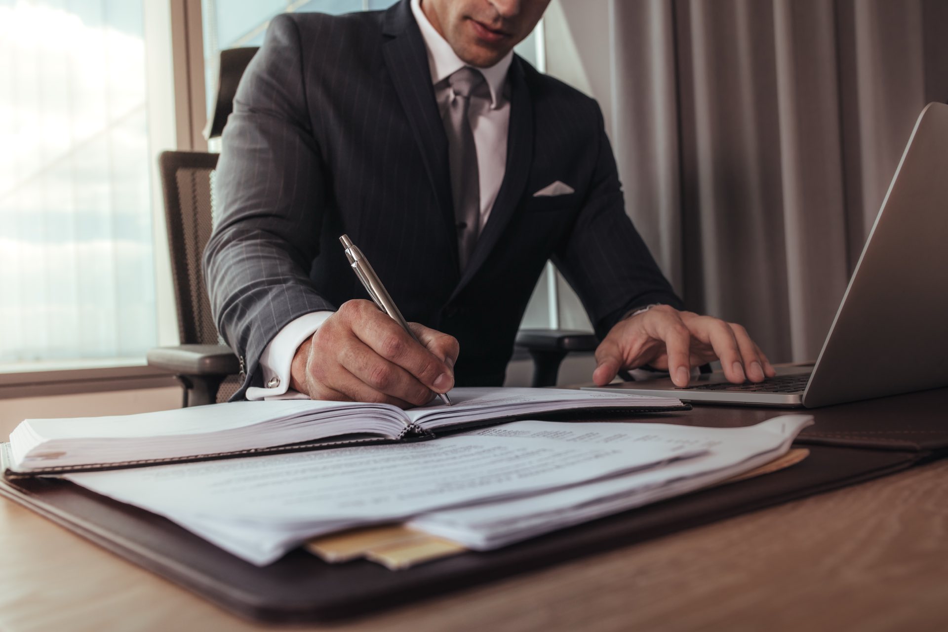 Man sitting at a desk in front of a laptop holding a pen filling out paperwork