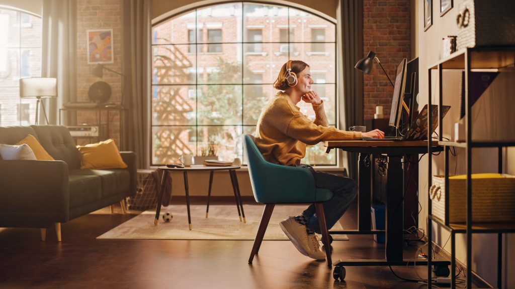A person sits at a desk with a large window next to them.